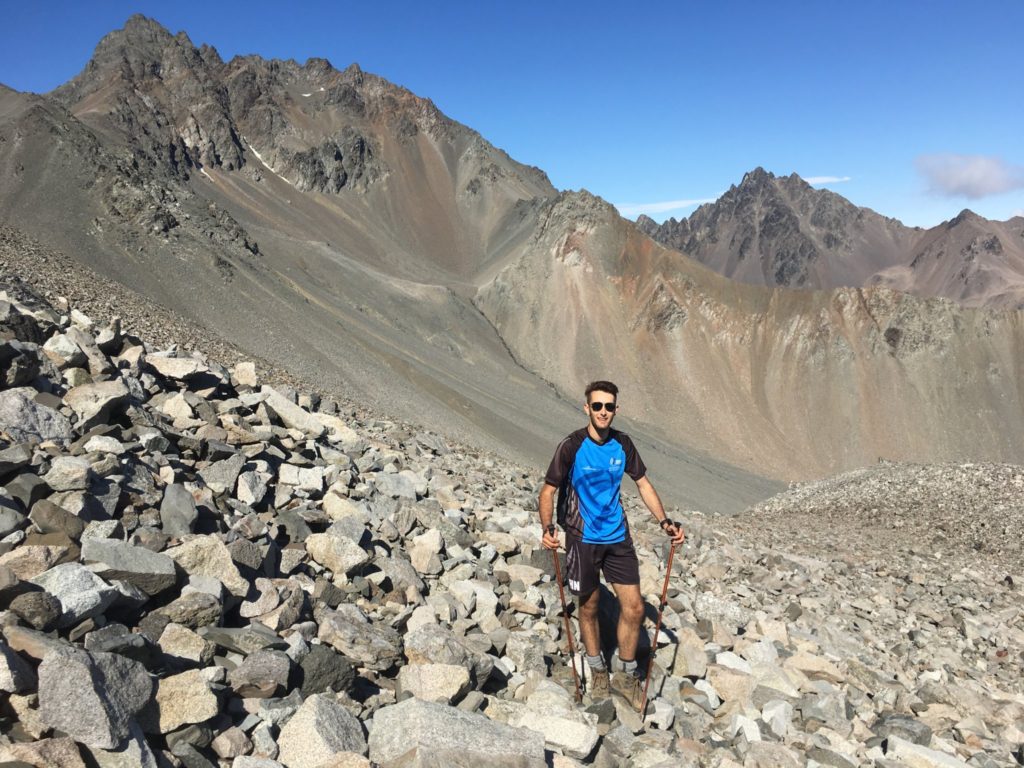 Mt. Alarm and Mt. Mitre in the background as Kane hikes up the rock scree